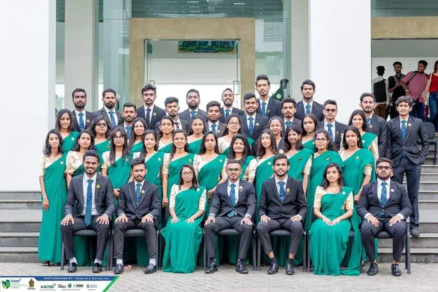 A formal committee portrait on the university steps: men in dark suits and blue ties, women in green sarees