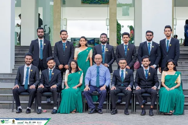 A smaller committee group in suits and green sarees, seated and standing on the steps around a senior staff member