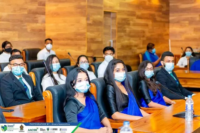 Committee members in masks seated at a wood-panelled council table with microphones