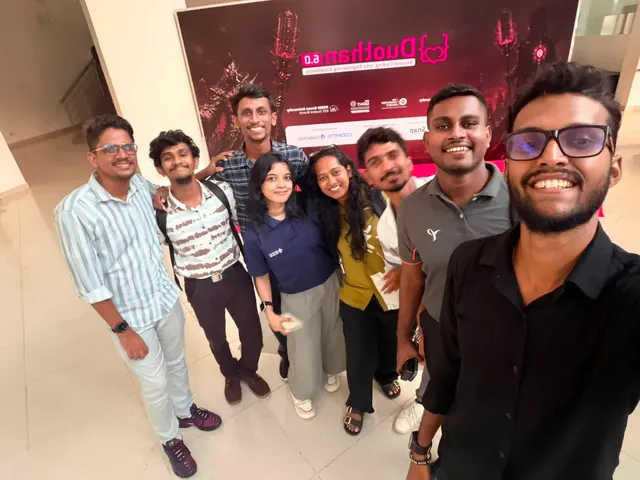 A selfie of eight organisers smiling in front of the Duothan 6.0 backdrop