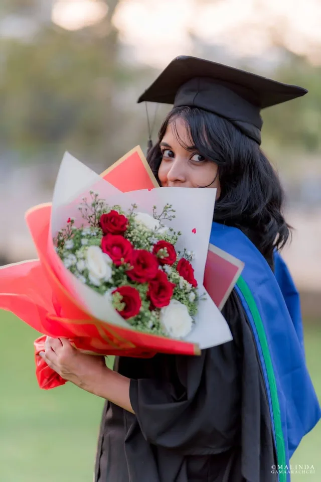 Wathsala in cap and gown, looking over her shoulder from behind a bouquet of red and white roses