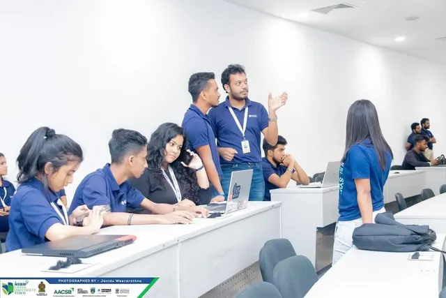 Volunteers in IEEE polos gathered around laptops in a lecture room, one of them explaining something