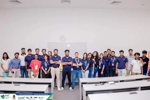 Around twenty-five IEEE Student Branch members, mostly in navy polos, posing in a lecture room